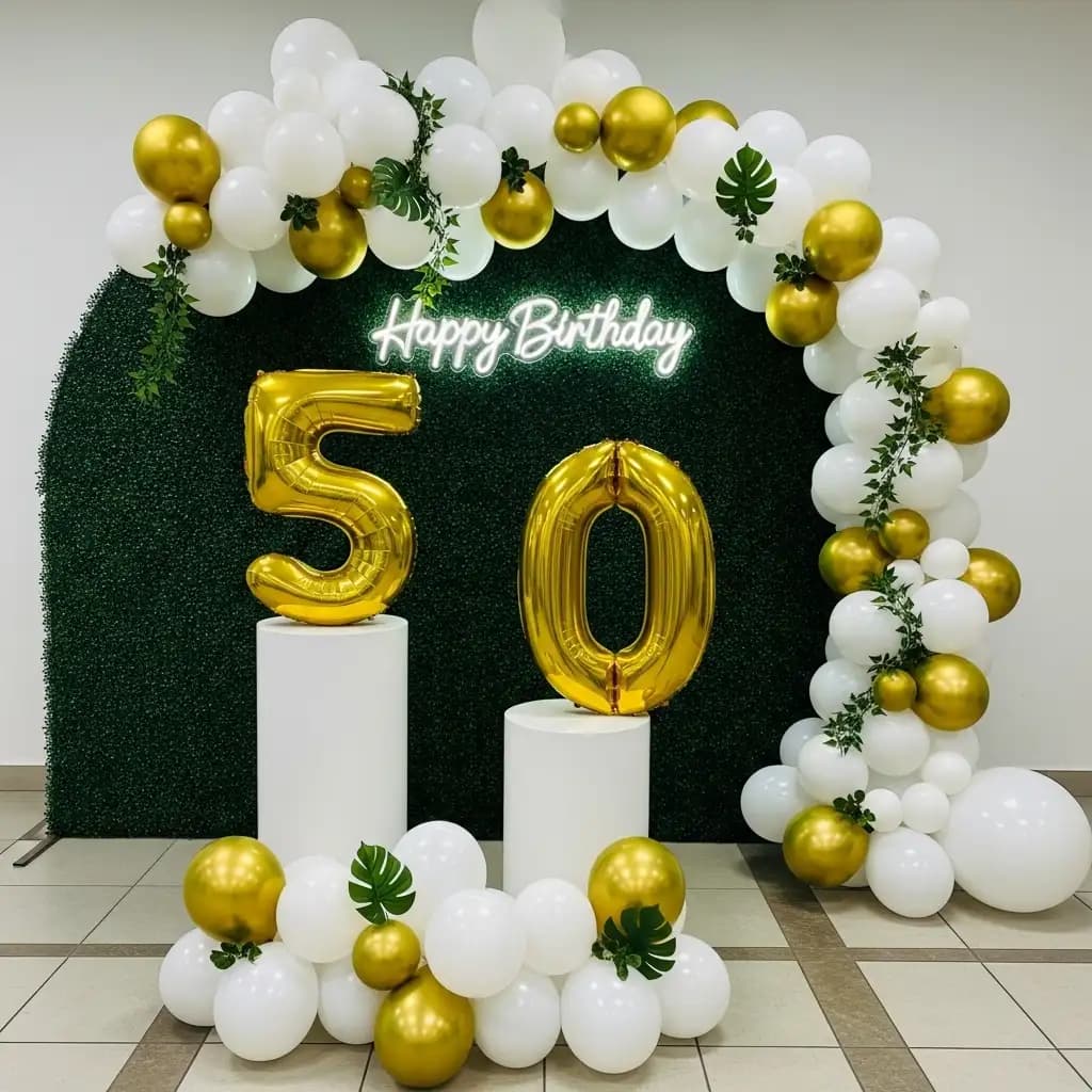 Elegant 50th birthday celebration featuring a lush green foliage backdrop with a glowing “Happy Birthday” neon sign, white pedestals holding gold “5” and “0” balloons, and classy balloon clusters in white and gold accented with greenery.